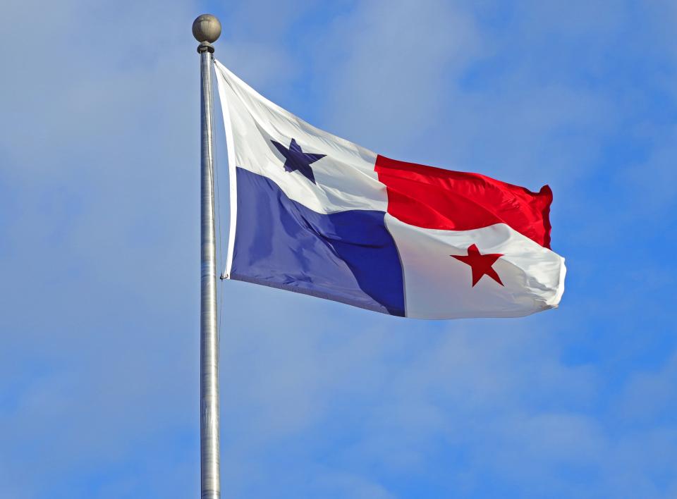 Country of Panama's flag flapping in the wind on a flagpole. Four squares, white with blue star, white with red star, solid red square, solid blue square. Blue sky behind.