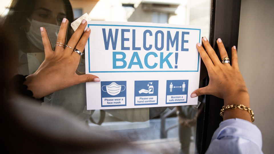 Business owner hanging "Welcome Back!" sign on business door