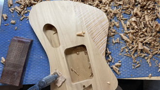a luthier carves a guitar from wood